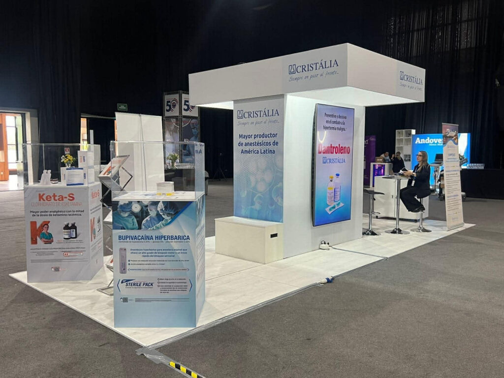 Un stand de Cristália en una feria muestra productos médicos y material promocional, con sillas, mostradores y pancartas en un gran recinto cubierto.