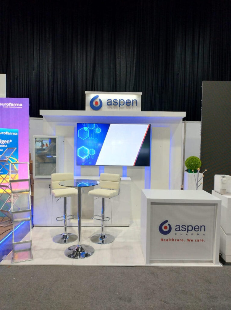 Stand de exposición de Aspen con logotipo, una pantalla digital, dos sillas blancas en una mesa alta y marca sanitaria.