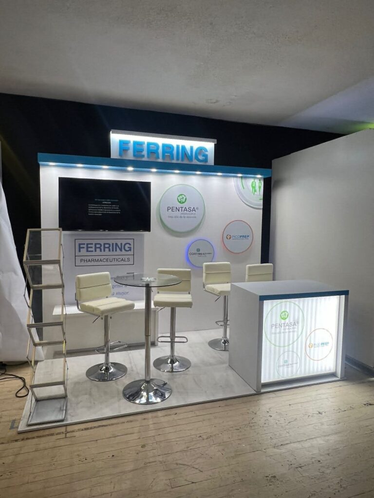 Stand de exposición para Ferring Pharmaceuticals con señalización de marca, pantalla de visualización, sillas altas, mostrador y material promocional sobre suelo de madera.