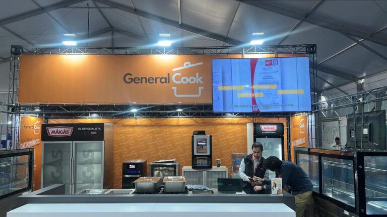 Un stand de feria de General Cook con electrodomésticos de cocina expuestos, dos personas hablando en el mostrador y un gran cartel naranja en lo alto.
