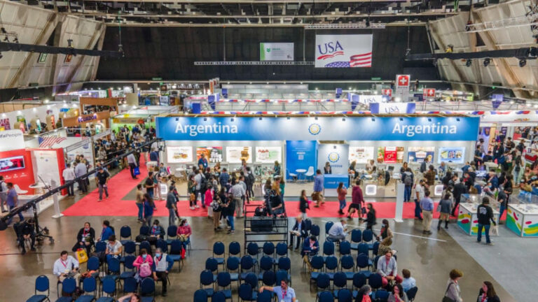 Una gran sala de convenciones cubierta con stands internacionales, incluidos los de Argentina y EE.UU., y filas de sillas con asistentes a un acto.